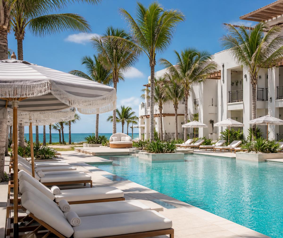 Sunlit pool deck of a white Southwest Florida beachfront resort with royal palms and the Gulf beyond
